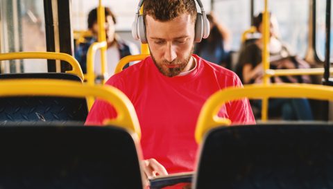 Young man listening to music, sitting in a bus, searching web.